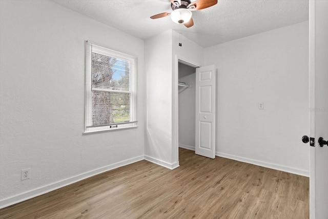 unfurnished bedroom with a textured ceiling, ceiling fan, baseboards, a closet, and light wood finished floors