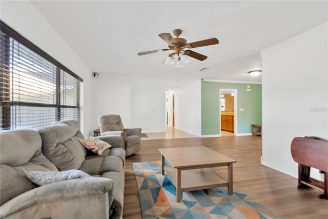 living area featuring a ceiling fan, ornamental molding, baseboards, and wood finished floors