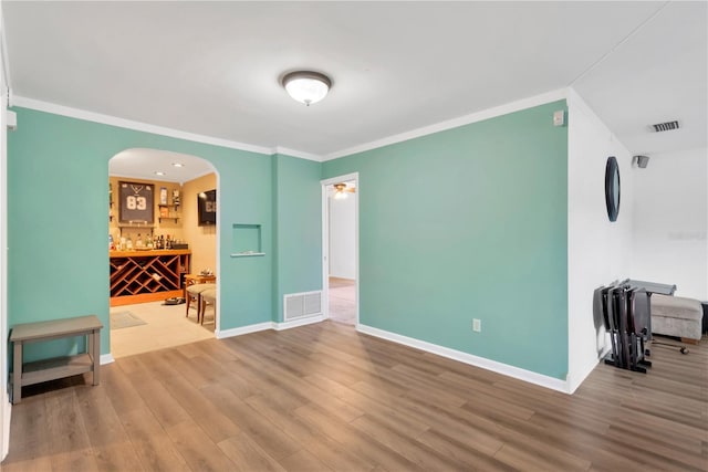 empty room featuring baseboards, crown molding, visible vents, and wood finished floors