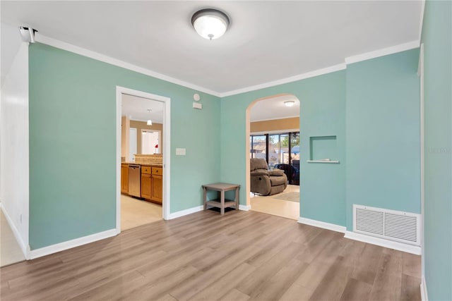 spare room with arched walkways, ornamental molding, visible vents, and light wood-style floors