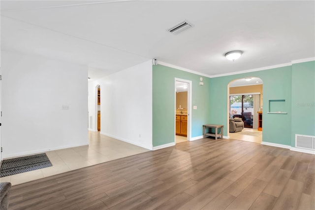 unfurnished living room with visible vents, arched walkways, and wood finished floors