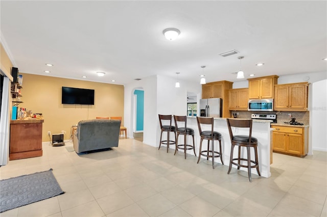 kitchen with arched walkways, a breakfast bar area, stainless steel appliances, visible vents, and decorative backsplash