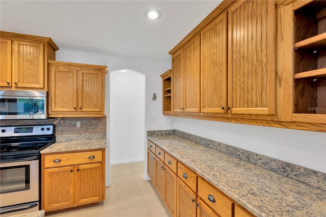 kitchen featuring stainless steel appliances, arched walkways, light stone counters, and open shelves