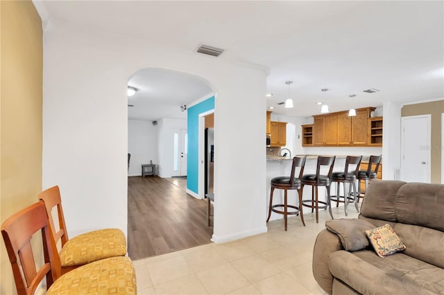 living room featuring visible vents, arched walkways, baseboards, ornamental molding, and light tile patterned flooring