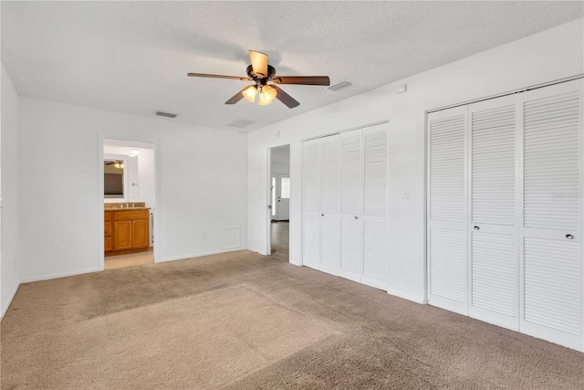 unfurnished bedroom with a textured ceiling, visible vents, two closets, and light colored carpet