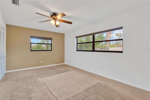 carpeted spare room featuring a ceiling fan, visible vents, a textured ceiling, and baseboards