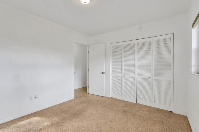 unfurnished bedroom featuring a closet, light colored carpet, and baseboards