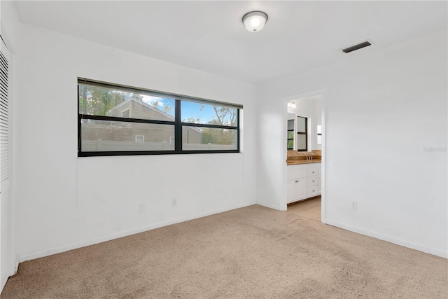 unfurnished bedroom with light carpet, ensuite bath, visible vents, and baseboards