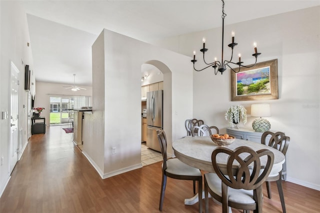 dining area with arched walkways, light wood-type flooring, a ceiling fan, and baseboards