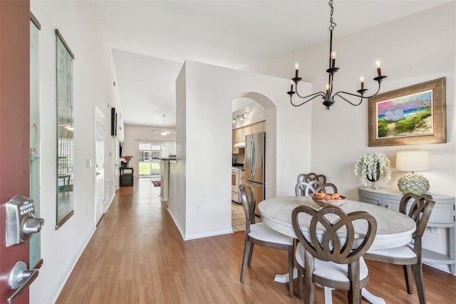 dining room with arched walkways, light wood-style flooring, baseboards, and ceiling fan with notable chandelier