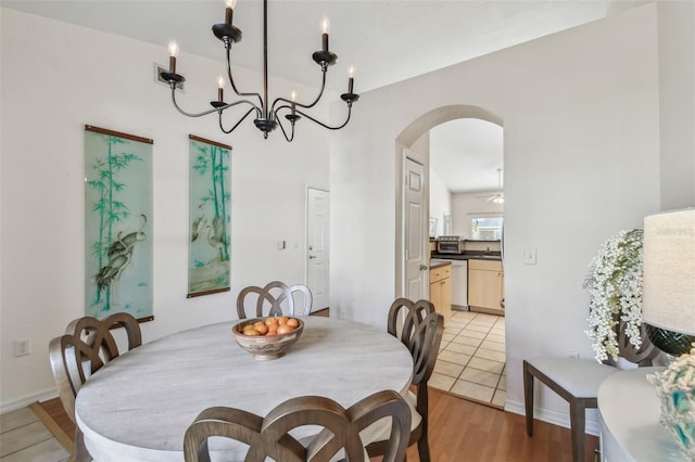 dining space featuring light wood finished floors, baseboards, arched walkways, and a notable chandelier