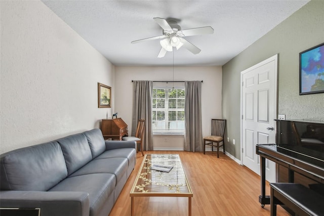 living room with light wood-style flooring, baseboards, a ceiling fan, and a textured wall