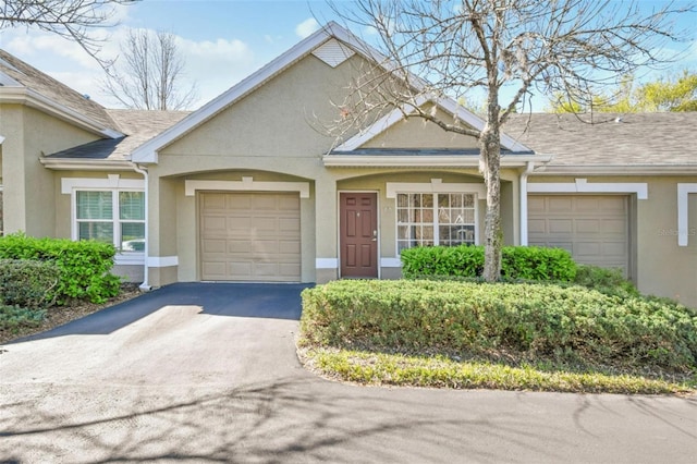 view of front facade featuring an attached garage, roof with shingles, aphalt driveway, and stucco siding