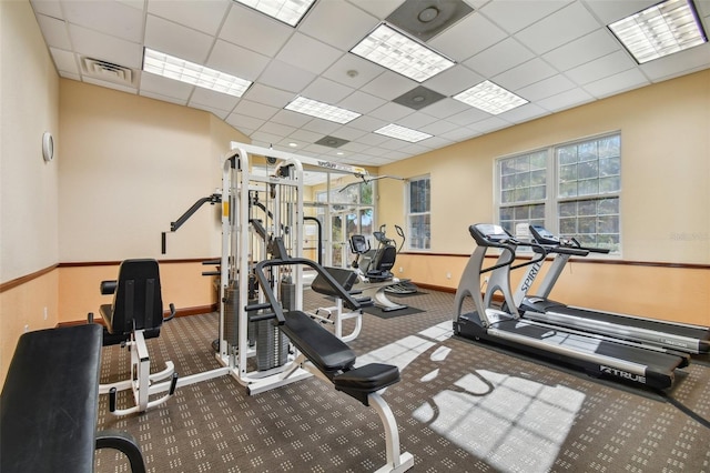 exercise room featuring a paneled ceiling, visible vents, and baseboards