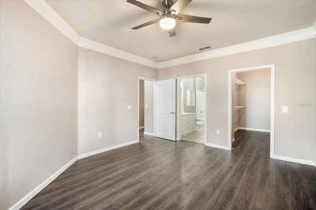 unfurnished bedroom featuring baseboards, visible vents, ornamental molding, dark wood-type flooring, and a walk in closet