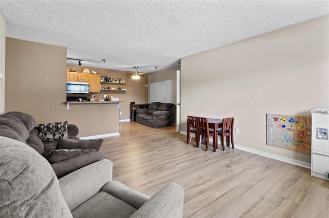 living area featuring a textured ceiling, light wood-type flooring, rail lighting, and baseboards