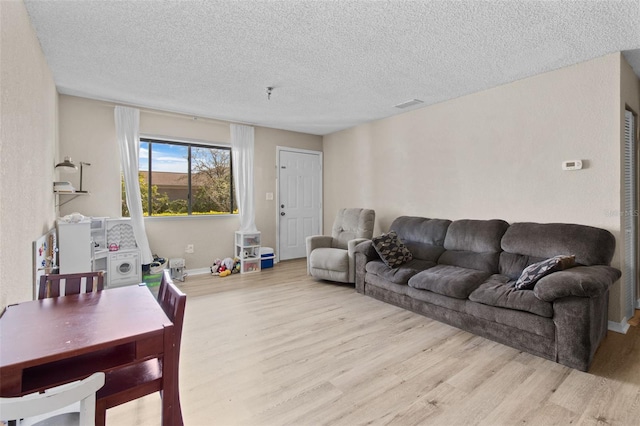 living room featuring baseboards, a textured ceiling, visible vents, and wood finished floors