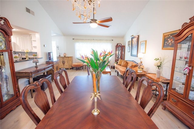 dining space featuring ceiling fan with notable chandelier, high vaulted ceiling, light wood finished floors, and visible vents