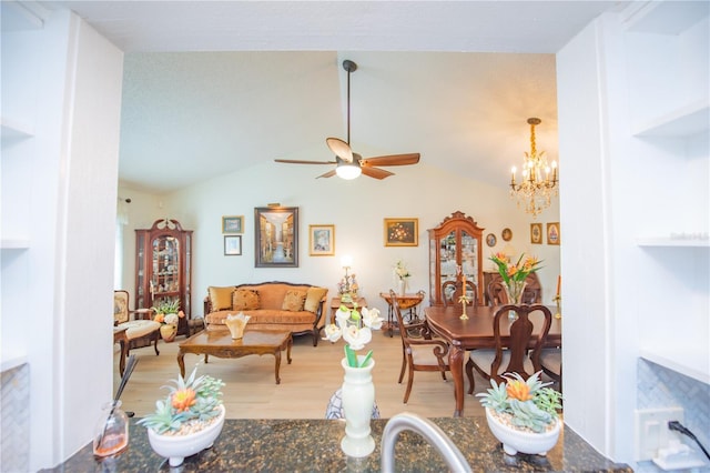 living room with vaulted ceiling, ceiling fan with notable chandelier, and light wood-style floors