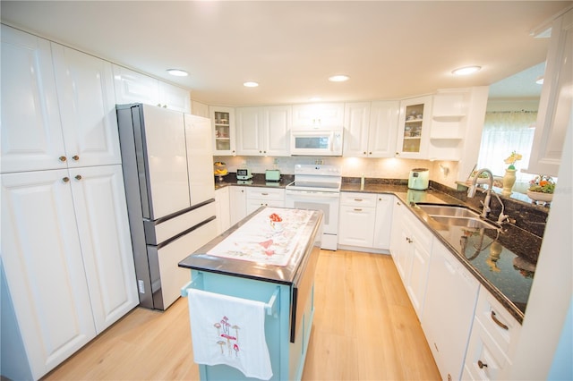 kitchen featuring white appliances, glass insert cabinets, light wood finished floors, and a sink