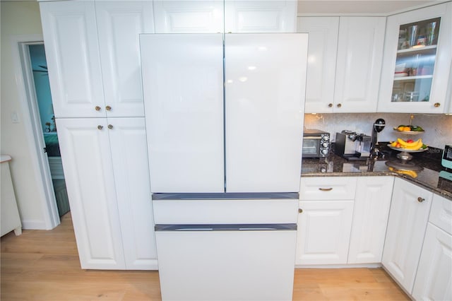 kitchen with white cabinetry, freestanding refrigerator, dark stone counters, light wood finished floors, and glass insert cabinets