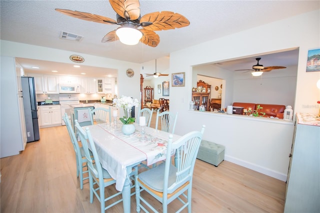 dining room with a textured ceiling, light wood-style flooring, visible vents, and baseboards