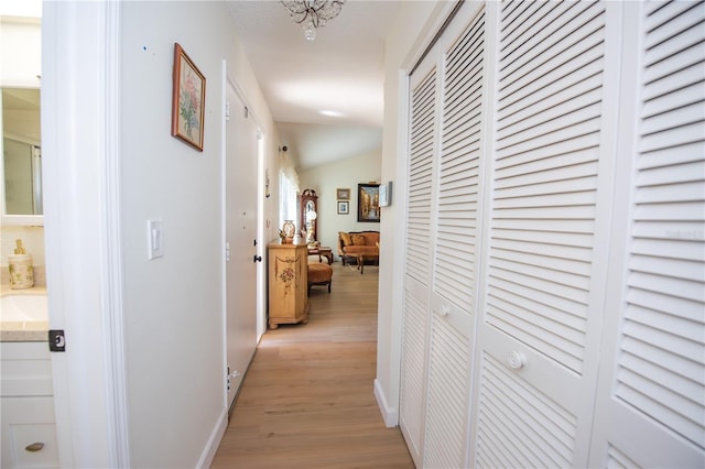 hallway with vaulted ceiling, light wood finished floors, and baseboards