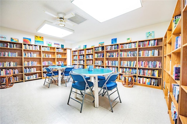 sitting room featuring wall of books, ceiling fan, and tile patterned floors