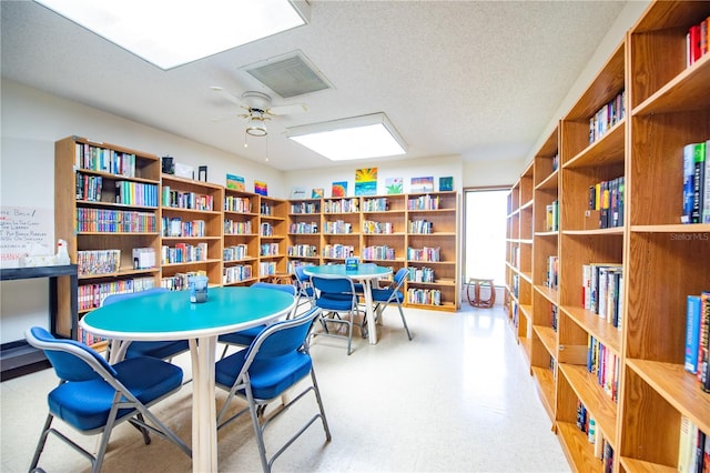 interior space with a textured ceiling, a ceiling fan, visible vents, wall of books, and tile patterned floors