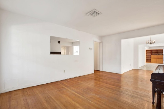 unfurnished living room with baseboards, wood-type flooring, visible vents, and an inviting chandelier