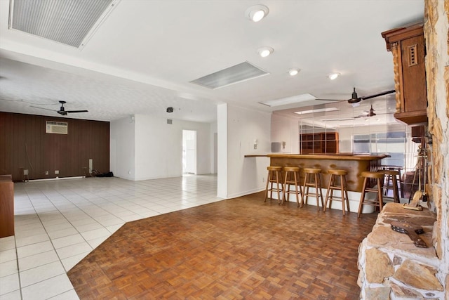 living room featuring wooden walls, visible vents, ceiling fan, tile patterned flooring, and a bar