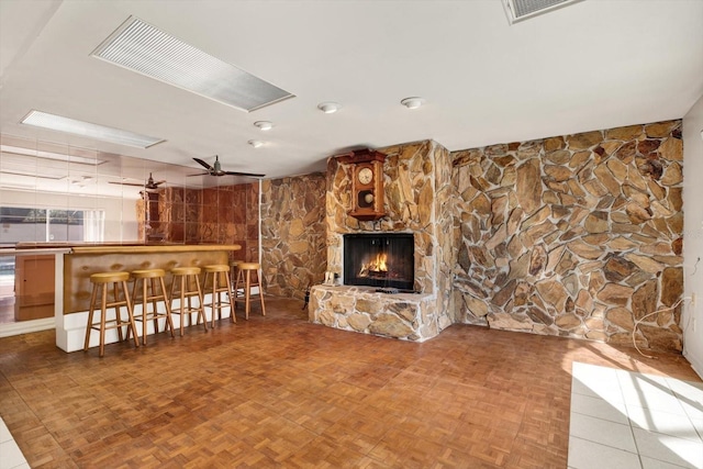 unfurnished living room featuring a ceiling fan, visible vents, a fireplace, and a bar