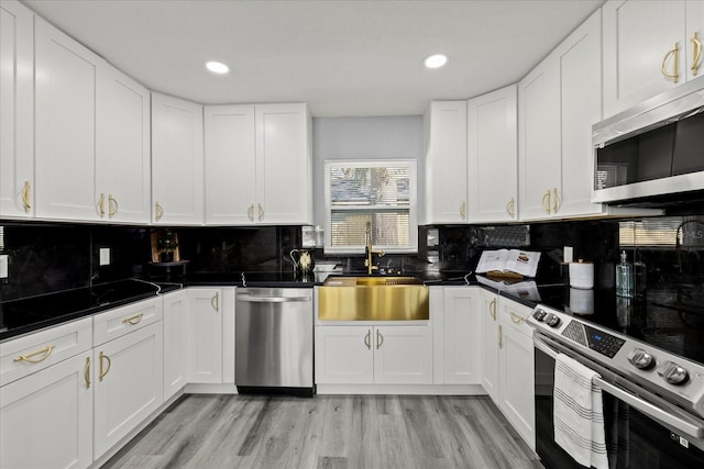 kitchen with dark countertops, a sink, stainless steel appliances, light wood-type flooring, and backsplash