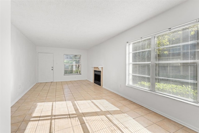 unfurnished living room featuring a fireplace, a textured ceiling, baseboards, and light tile patterned floors