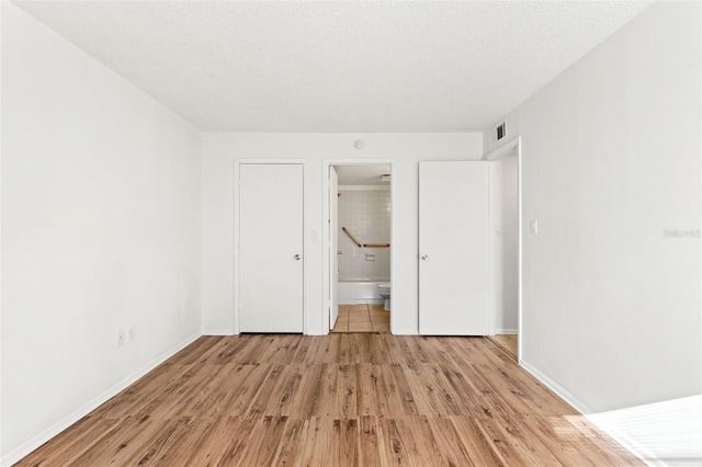 unfurnished bedroom featuring light wood finished floors, baseboards, visible vents, ensuite bathroom, and a textured ceiling