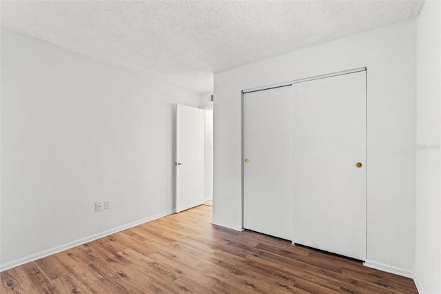 unfurnished bedroom with a closet, a textured ceiling, baseboards, and wood finished floors