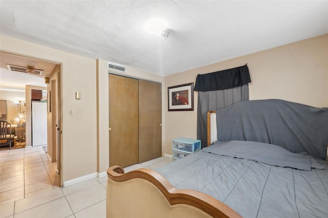 bedroom with light tile patterned floors, baseboards, visible vents, freestanding refrigerator, and a closet