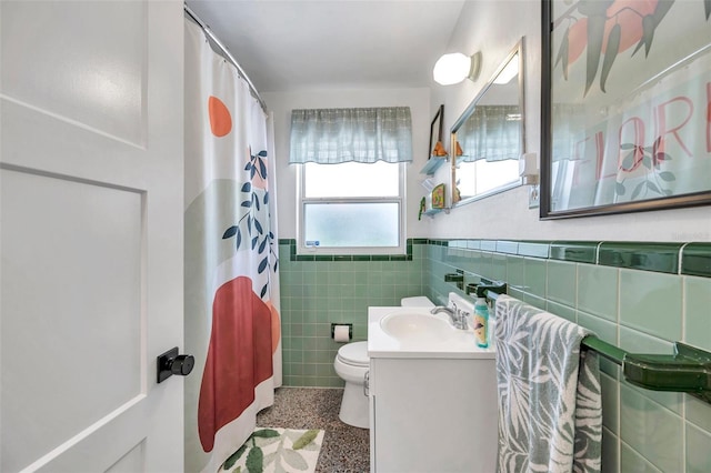 bathroom with toilet, speckled floor, vanity, tile walls, and wainscoting