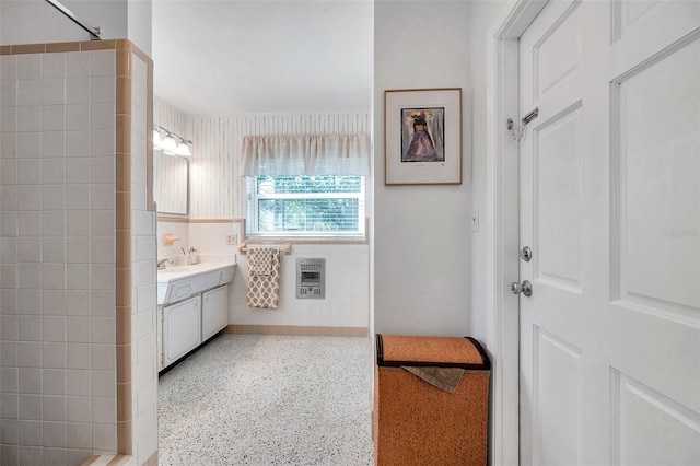 bathroom with speckled floor, tiled shower, vanity, and heating unit