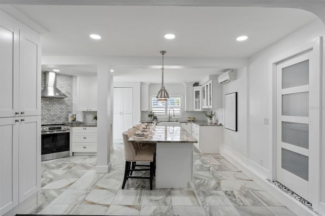 kitchen featuring wall chimney exhaust hood, glass insert cabinets, stainless steel range with electric stovetop, white cabinetry, and a wall mounted AC