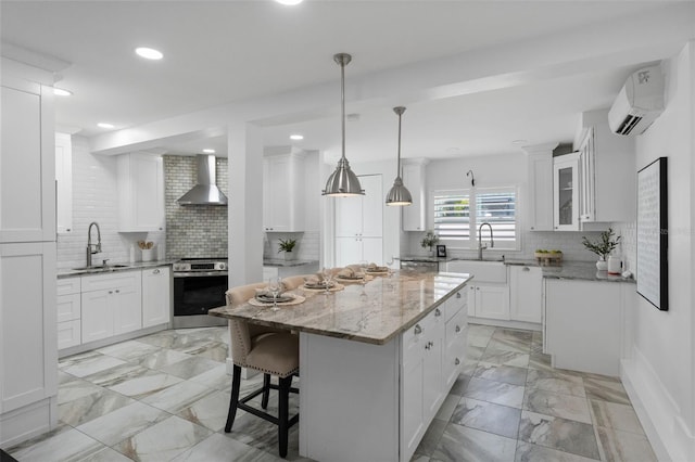 kitchen with marble finish floor, stainless steel electric stove, an AC wall unit, a sink, and wall chimney range hood