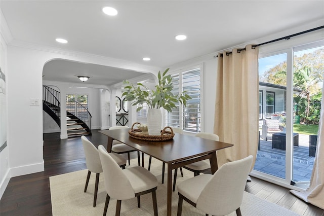 dining room featuring arched walkways, dark wood-style flooring, crown molding, baseboards, and stairs