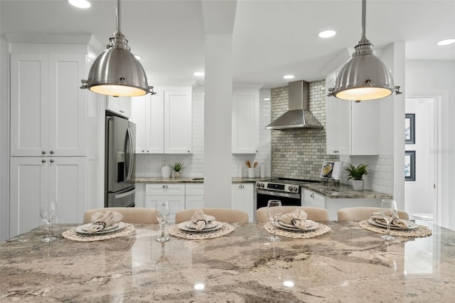 kitchen featuring wall chimney exhaust hood, appliances with stainless steel finishes, white cabinets, and pendant lighting