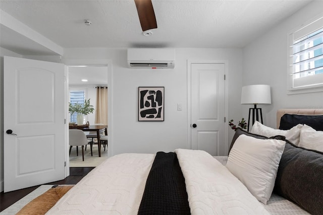 bedroom with ceiling fan, dark wood-style flooring, a wall unit AC, and a textured ceiling