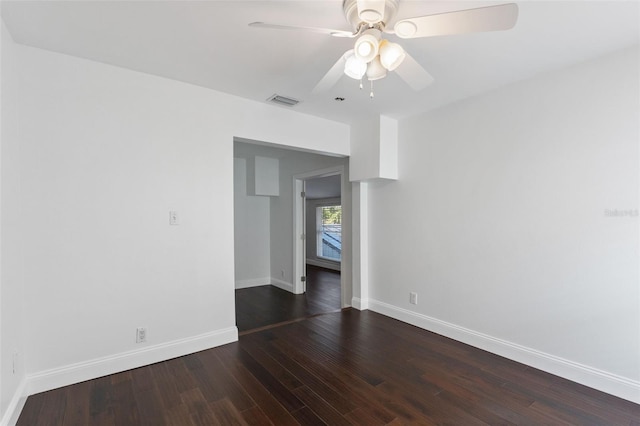 spare room featuring dark wood-type flooring, a ceiling fan, visible vents, and baseboards