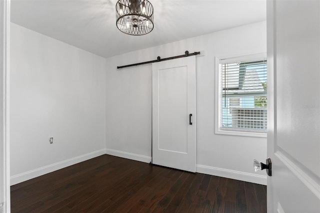 unfurnished bedroom featuring a barn door, baseboards, a chandelier, and dark wood-style flooring