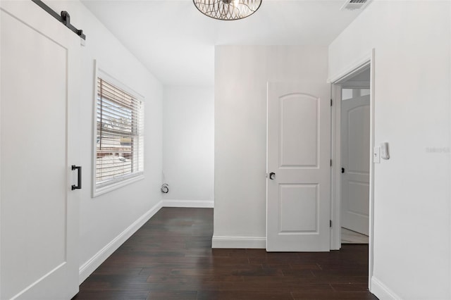 hallway with a barn door, visible vents, baseboards, and wood finished floors