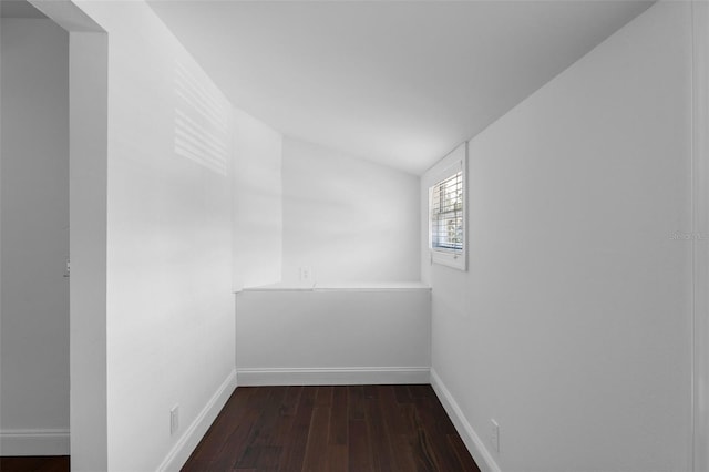 empty room featuring lofted ceiling, wood-type flooring, and baseboards