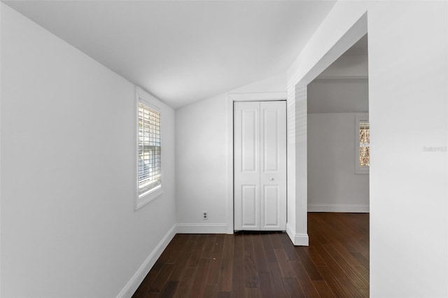 unfurnished bedroom featuring dark wood-type flooring, lofted ceiling, a closet, and baseboards