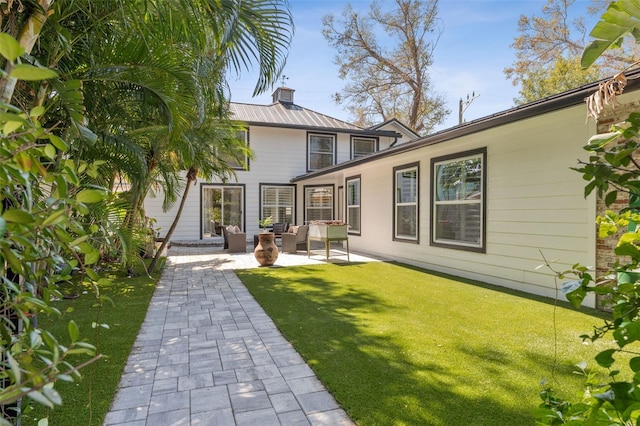 rear view of house with a chimney, metal roof, a lawn, and a patio